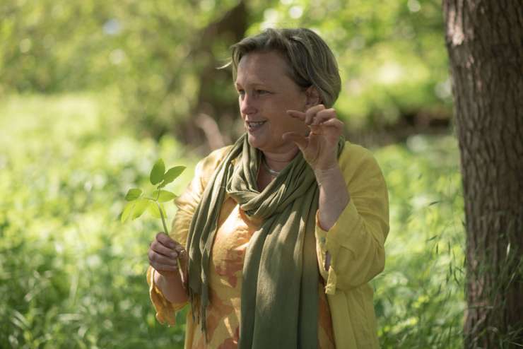 Simone Schäfer steht in grüner Natur. In der rechten Hand hält sie ein Giersch-Blatt, mit den Fingern der linken Hand zeigt sie, wie klein diese Blätter am Anfang sind.